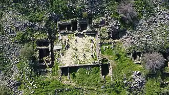 Aerial drone view of the synagogue at Khirbet Wadi Hammam, with its walls, column bases and adjoining rooms visible amid vegetation and rubble on the hillside
