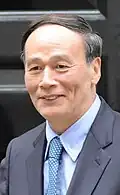a smiling nearly bald man, wearing a suit and a blue tie
