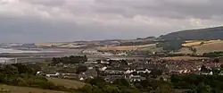 View of multiple houses with sea on the left and hills in the background.