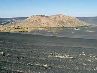 A white hill within a black depression, with lakes and vegetation at its foot and desert elsewhere