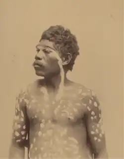 Portrait photograph of a shirtless Aboriginal man with decorative panting on his torso