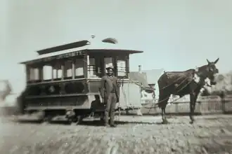 Griffon stands in front of a wooden streetcar, which is tethered to a mule