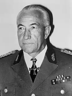 A black-and-white photograph of a man wearing a black military uniform, peaked cap and a neck order in shape of an Iron Cross.
