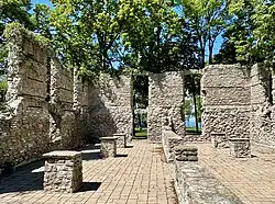 Interior of the ruined limestone structure, showing remaining walls, and a brick floor. There are openings in the walls where windows once were, with trees and Lake Erie visible in the background through the openings.