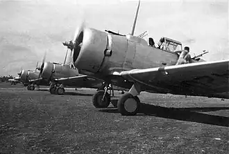 Row of single-engined military monoplanes on airfield, propellers spinning