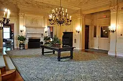 A large carpeted lobby with a center table, fireplace, and chandelier