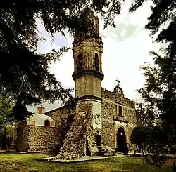 Photograph through the trees showing the outside of a church with with a tall tower on one side