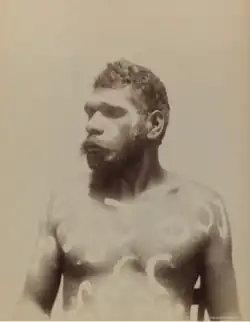 Portrait photograph of an Aboriginal man with decorative painting on his torso