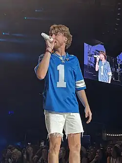 Bailey Zimmerman, dressed in a sports jersey and shorts, singing into a microphone