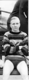 George Burleigh, sitting on a bench wearing his swimming trunks and a striped sweater.