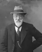An elderly bearded man in a light hat wearing a suit