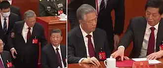 alt=Left: Hu (in light grey hair) questioning Xi Jinping as he is escorted out Right: Li Zhanshu taking a file away from Hu as staff approaches