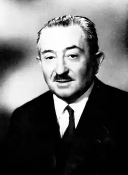 A middle-aged man in a suit with slicked back hair and a small mustache