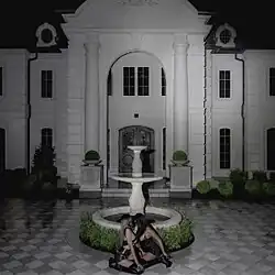 Two women sitting by a fountain in front of a large white mansion