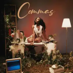 Starr seated on a white desk in a studio decorated with plants and flowers, wearing a pastel pink outfit and looking upward, with the word "Commas" written above her in cursive.