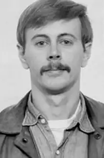 Black-and-white headshot of a man with short hair and mustache wearing a jacket over a collared shirt, looking directly at the camera