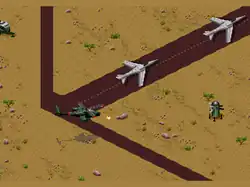 A square-shaped video game screenshot that is a digital representation of military airstrip in the desert. A green helicopter fires projectiles at a stationary green device with guns. Two grey fighter jets are on the airstrip.