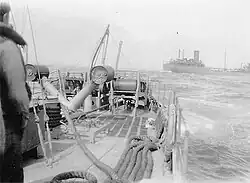 An oil tanker is half-visible just behind the stern of Dione; the tanker is partially cut out by the camera's frame