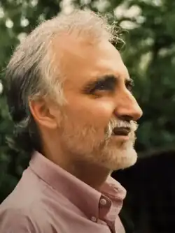 Head and shoulders profile view of Fowler, a man in middle age, wearing an open-necked shirt. He has collar-length grey hair and a neat grey beard.