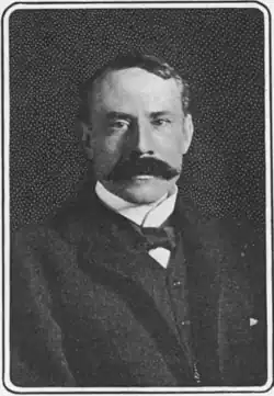 Middle-aged white man with dark hair and large moustache, facing the camera