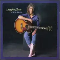 full-length photo of Emmylou Harris in blue pants and top and white boots perched on a black stool holding a guitar
