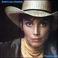 head and shoulders photo of Emmylou Harris looking directly at viewer wearing straw western hat, covered neck, and jacket