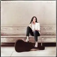 photo of Emmylou Harris in white shoes sitting on a depot bench with guitar in case