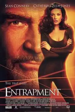 A woman in tight fitting bodysuit, crisscrossed laser beams in front of her, behind the looming face of an older gray-bearded man.