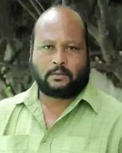 indian male, bald and with a full beard, wearing a dayglow-green hawaiian shirt