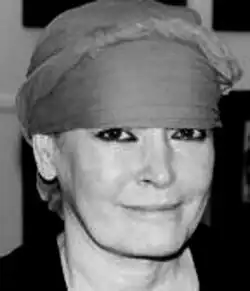 Black and white Press publicity shot of a smiling woman with heavy eye makeup, wearing a headscarf.