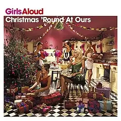 Five members of British pop group Girls Aloud in festive red and white outfits, posing in a stylized retro kitchen with a Christmas tree and wrapped presents.