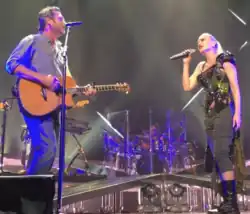 A color picture of singer Gwen Stefani and Blake Shelton performing the aforementioned song live.