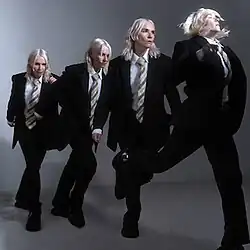 A composited timelapse image of a white-haired woman wearing a suit, in which she moves to the right and towards the camera.