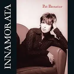 rust and black duotone photo of Pat Benatar gazing at camera seated with legs up in corner of cushioned leather couch