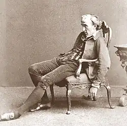 middle aged, clean-shaven white man with collar-length hair slumped in a chair