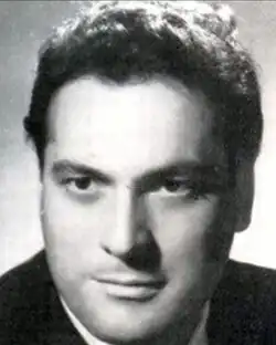 Black and white studio publicity shot of an unsmiling, clean-shaven man with short, curly, dark hair, brushed back.