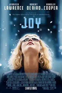 A blonde woman wearing sunglasses, her head tilted back and snow falling.