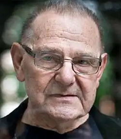 Colour Press shot of an elderly, unsmiling man with spectacles and short, receding, grey hair.