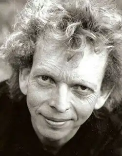 Black and white publicity shot of a smiling man looking upwards at the camera. He is clean-shaven, and has curly, windblown, greying hair.