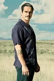 A man stands in the desert in broad daylight, menacingly looking at the camera