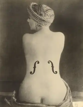 A photo depicting Kiki from the back, nude to below her waist, with two f-holes painted on her body to resemble a violin.