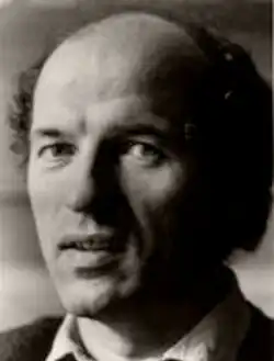 Studio, three-quarter profile, black and white publicity shot of a clean-shaven, unsmiling man with the beginnings of premature balding, and dark, curly hair.