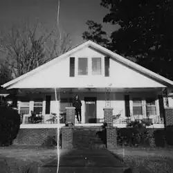 Black and white image where MJ Lenderman stands on the porch of a house