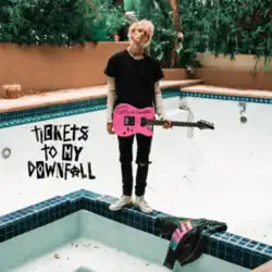 Bleached-blonde young man wearing skinny jeans, holding pink electric guitar, standing on the edge of a drained pool/jacuzzi outside
