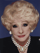 Photograph of woman with curly white hair wearing a black garment and a gem as a necklace