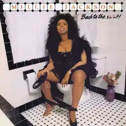 A woman in a black dress holding her shoe as she strains herself while seated on a toilet. The text "Millie Jackson" and "Back to the S**t!" stand above her.