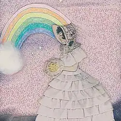 A woman carrying what appear to be flowers, wearing a white dress, in front of a pink background and a rainbow
