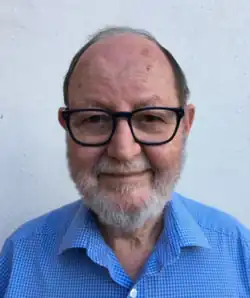 A balding man with a short white beard in a blue and white checkered shirt