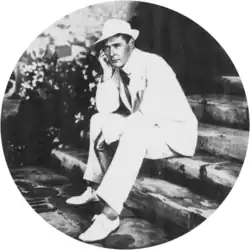youngish, clean-shaven white man in a light-coloured suit, seated on a garden step, looking pensive