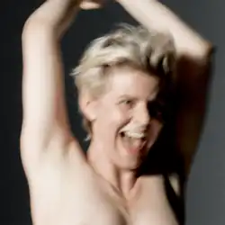 A picture of Robyn smiling with her arms raised while topless